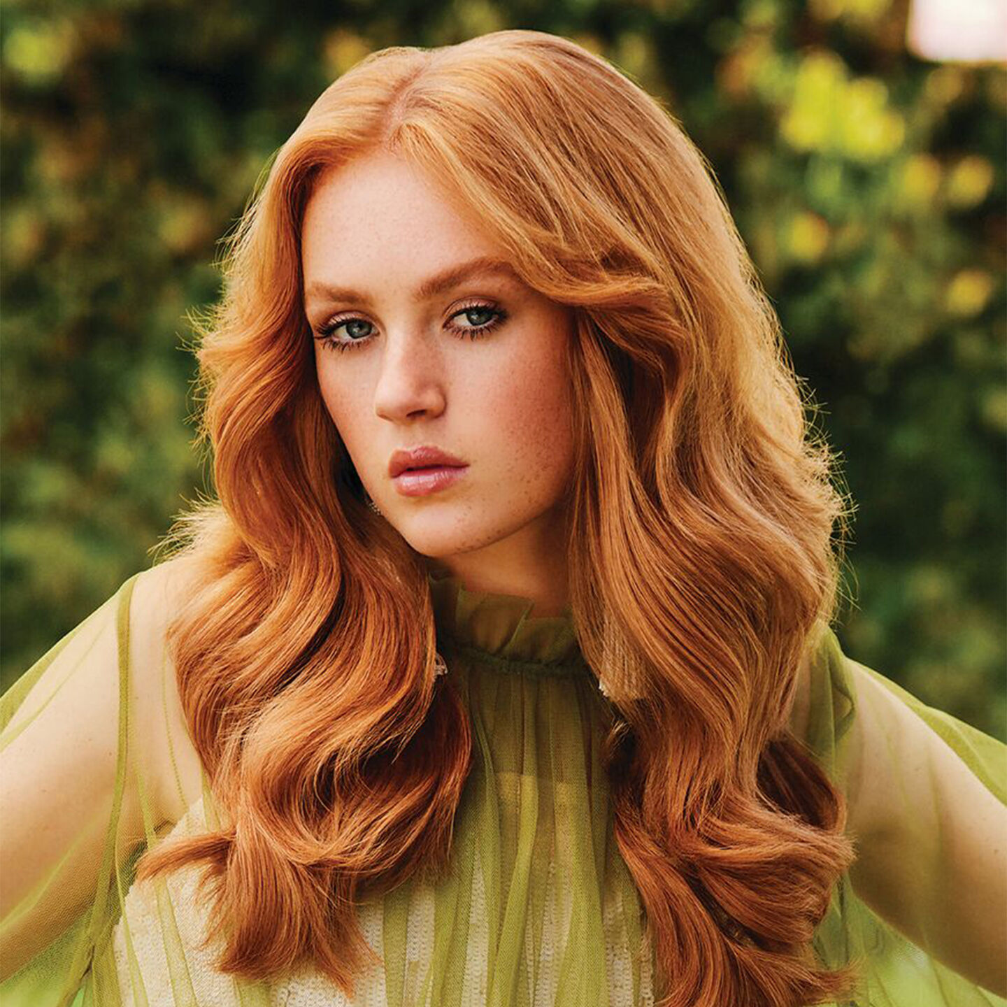 Femme aux cheveux rouges avec des boucles douces et fluides drapées sur un haut vert citron transparent, mettant en valeur une coiffure simple mais élégante.